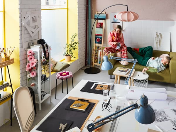 Un espace de travail/salon décoré dans des couleurs éclatantes, avec deux jeunes femmes s’accordant une pause sur un canapé KLIPPAN.