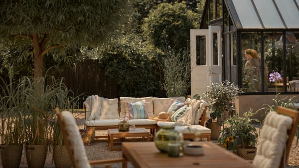 Un espace extérieur avec un canapé modulaire d’extérieur brun clair avec des coussins beiges, plus une table d’extérieur brun clair avec un fauteuil à dossier réglable.