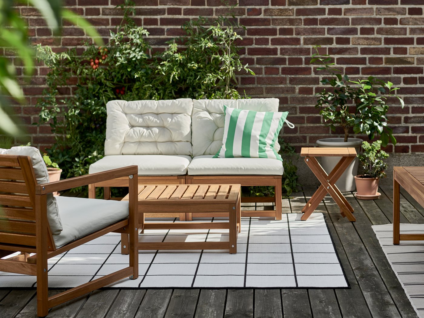 Un espace extérieur ensoleillé avec un ensemble quatre places NÄMMARÖ sur un tapis, et des plantes contre un mur de briques.