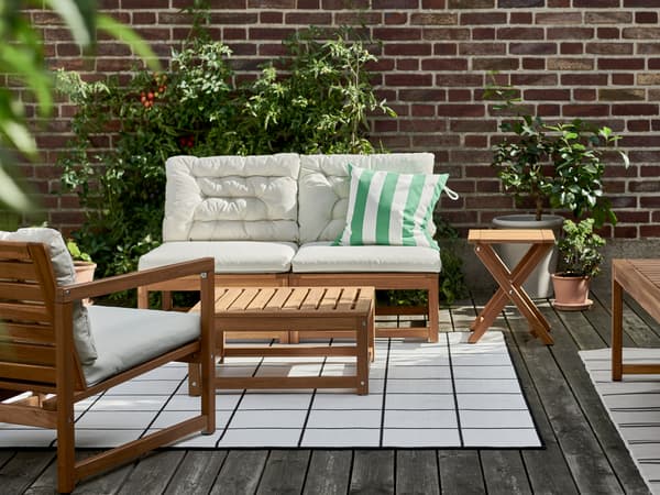 Un espace extérieur ensoleillé avec un ensemble quatre places NÄMMARÖ sur un tapis, et des plantes contre un mur de briques.