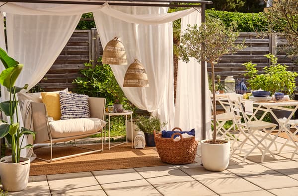 Un espace extérieur tout en beige, jaune et bleu avec des oliviers et des plantes vertes.