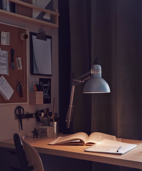 Un espai de treball lleugerament il·luminat amb un llum i llibres a l'escriptori.
