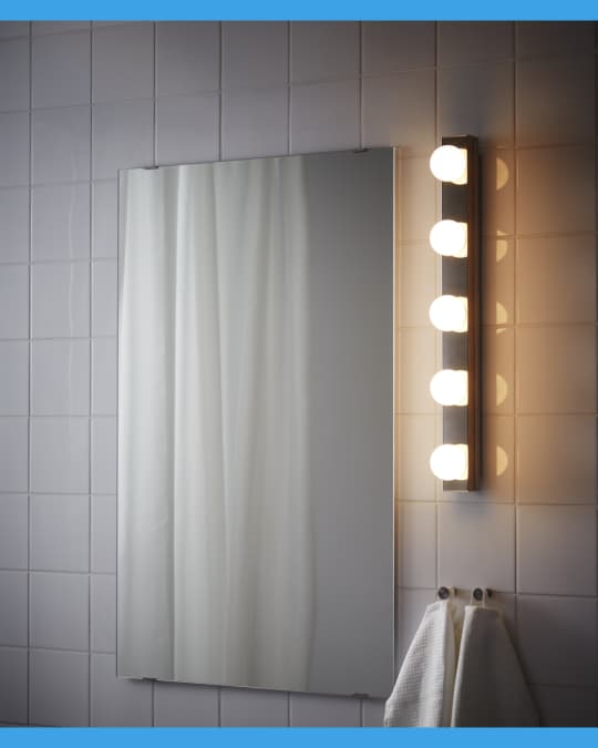 Un espejo de baño y al cosado un set de luces para baño encendidas.