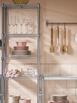 Un estante de metal con platos y vasos de vidrio en una pared rosa con azulejos.