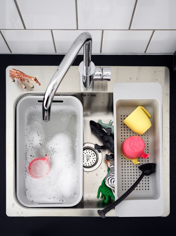 Un évier et une bassine GRUNDVATTNET blanche avec de l’eau savonneuse et des figurines d’animaux attendant le bain.