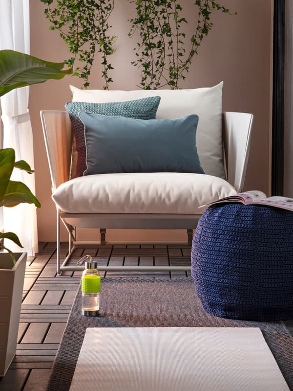 Un fauteuil blanc orné de coussins gris sur un sol en bois, un tapis devant lui et une fenêtre sur le côté.