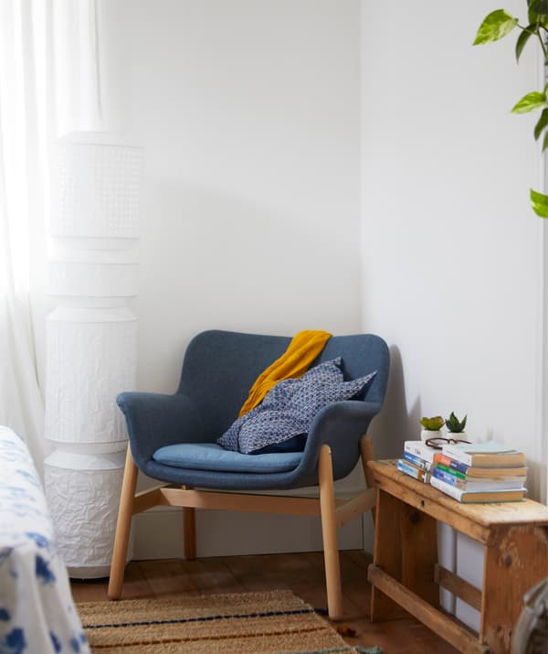 Un fauteuil bleu dans le coin d'une pièce blanche et un lampadaire en papier.