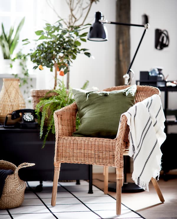 Un fauteuil en rotin et en bambou avec un coussin vert et un jeté rayé.