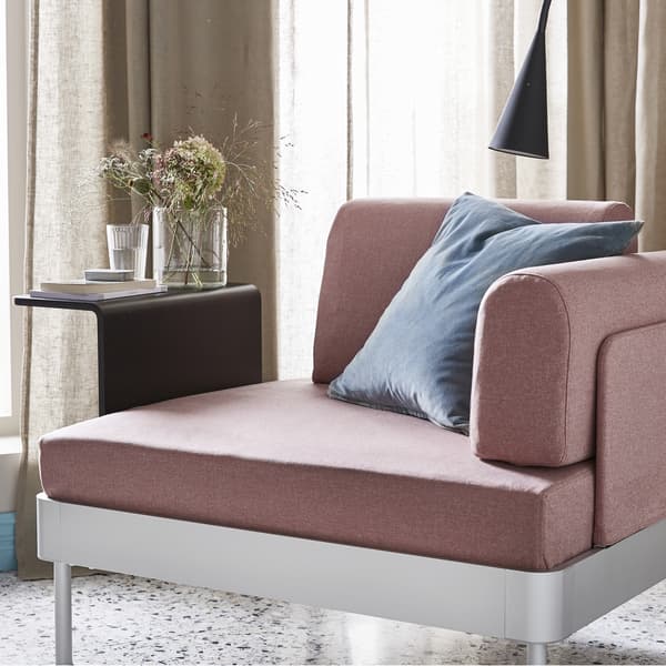 Un fauteuil rose pâle et une table d’appoint noire avec un vase de fleurs.
