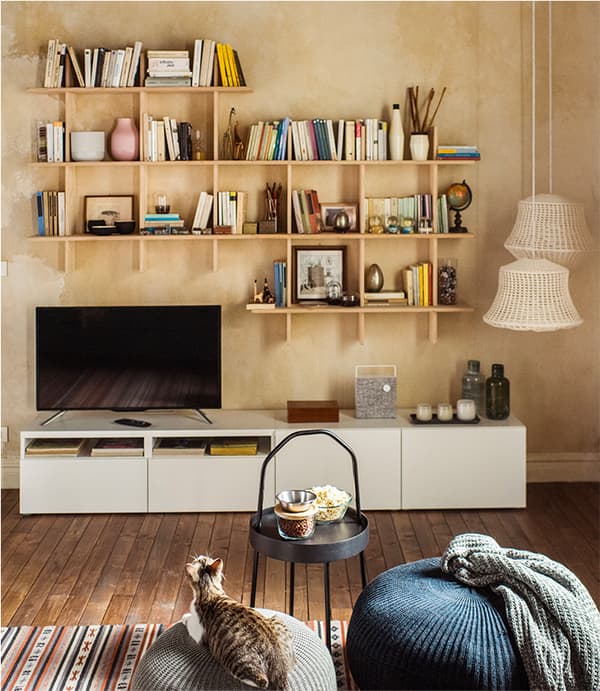 Un gatto in un soggiorno seduto su un pouf grigio SANDARED. Di fronte, un tavolino nero BURVIK con ciotoline. Sulla parete di fondo pensili e una parete TV BESTÅ.
