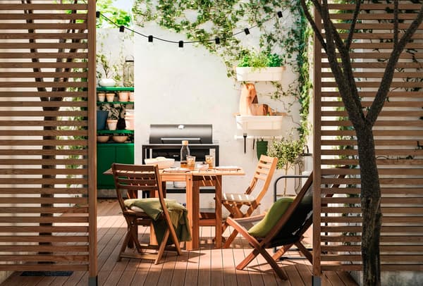Un giardino illuminato dal solo con un tavolo e due sedie NÄMMARÖ. In fondo c'è una brace da barbecue.