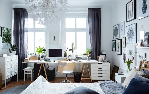 Un gran dormitorio branco cun espazo de oficina en casa, fronte a grandes fiestras.