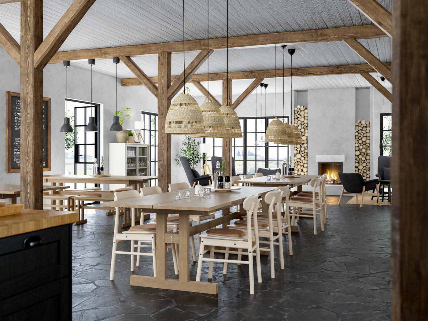 Un grand espace rustique aux poutres en bois et au sol en pierre avec des tables, des chaises et des suspensions en bois clair et en matériaux naturels.