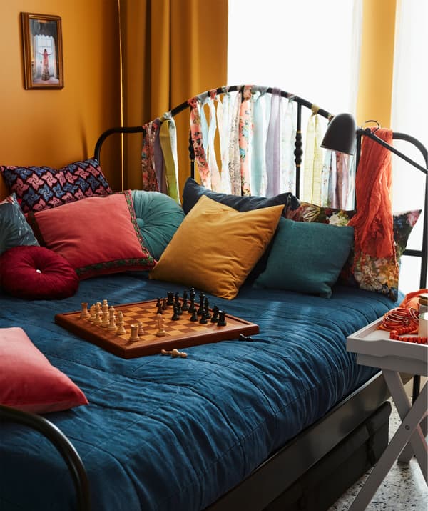 Un grand lit coloré sur lequel sont disposés beaucoup de coussins et un jeu d'échecs. Une table plateau avec des rafraîchissements à côté du lit.