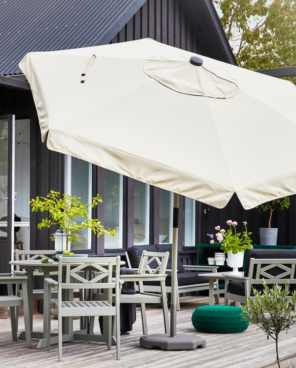Un grand parasol beige est installé près de la zone repas de la terrasse: une table et quatre chaises en finition grise.