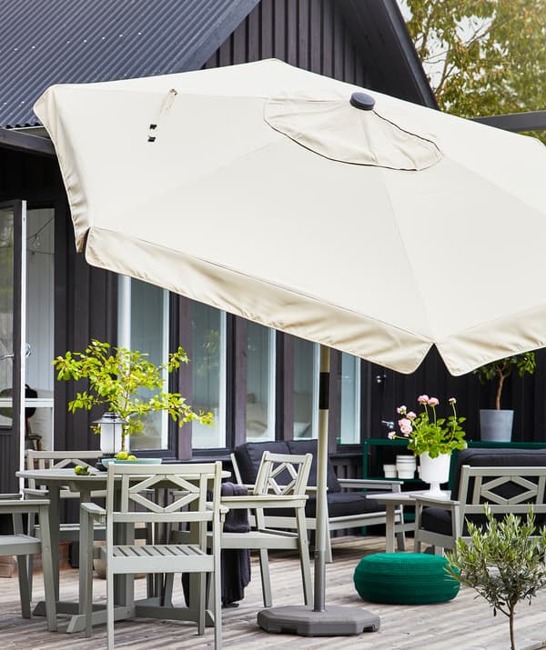 Un grand parasol beige sur une terrasse avec des meubles d’extérieur gris et des plantes.