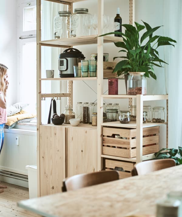 Un grand rangement en bois dans une cuisine/salle à manger avec des bocaux en verre, des caisses en bois et des accessoires de cuisine sur les étagères.