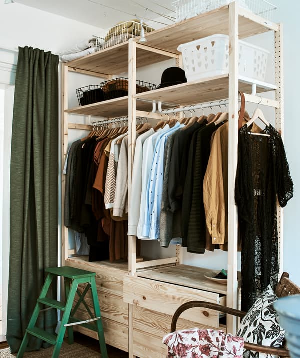 Un grand rangement en bois pour vêtements avec tiroirs, une tringle à vêtements, des étagères pour les boîtes et un tabouret vert dans le coin.