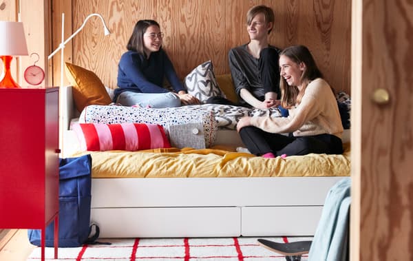Un groupe d’adolescents discute, assis sur un lit avec lit tiroir SLÄKT dans une chambre à coucher aux murs revêtus de panneaux de bois.