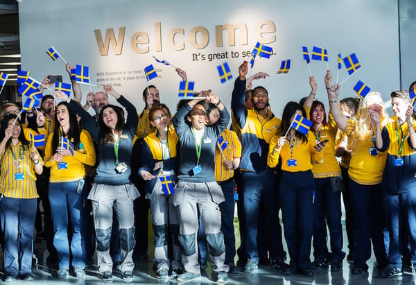 Un groupe de collaborateurs IKEA agitant le drapeau suédois devant un panneau Welcome.