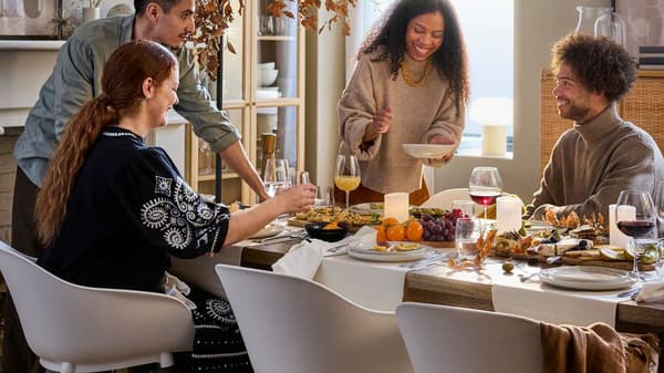 Un groupe rassemblé autour d’une grande table à manger en bois couverte de décorations sur le thème de l’automne et des chaises de salle à manger blanches.
