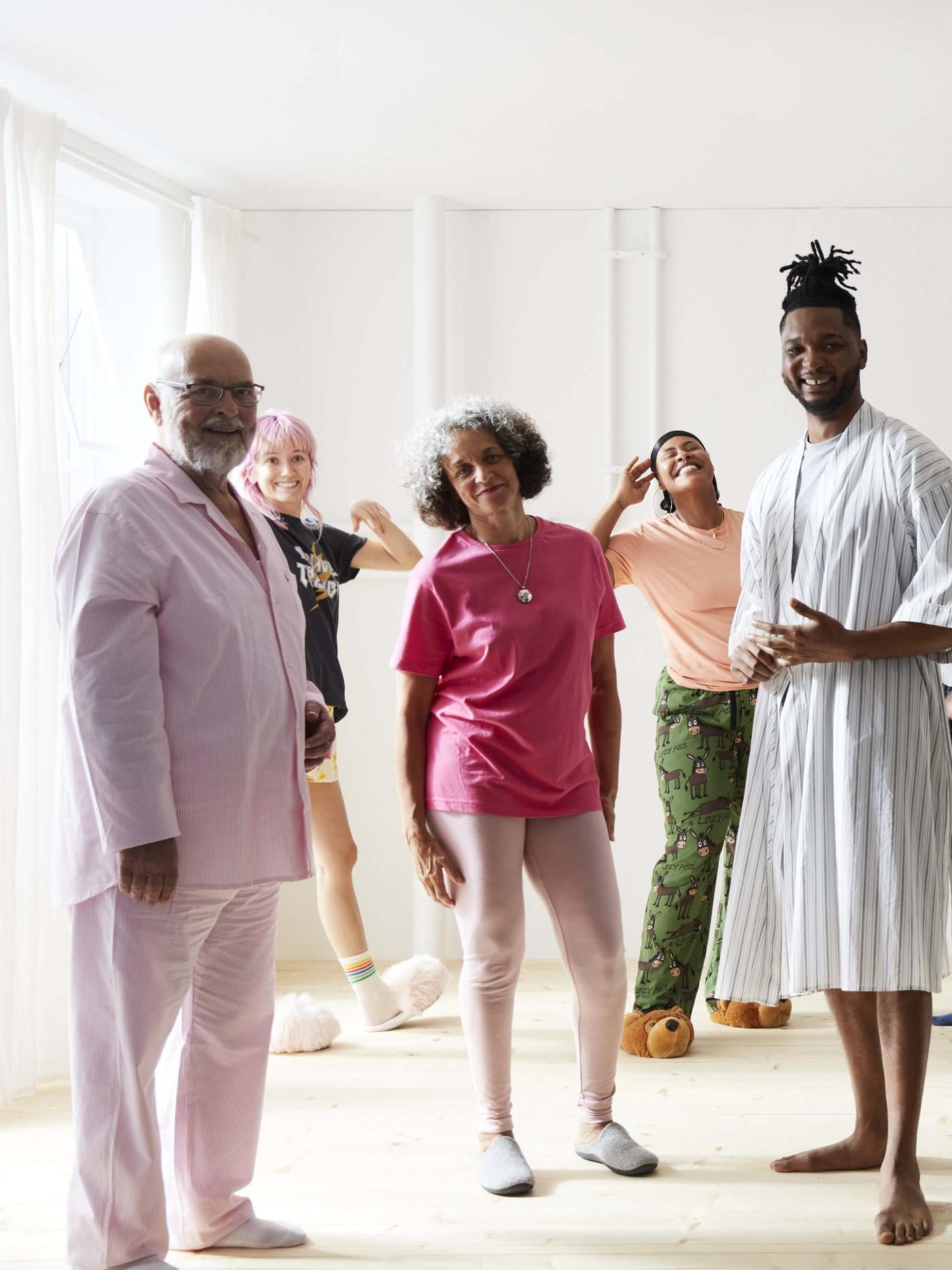 Un grupo de personas vestidas con sus pijamas, todas de pie en una habitación luminosa, sonriendo.