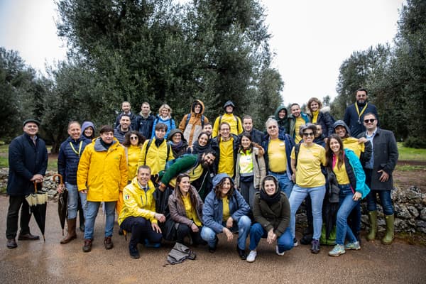 Un gruppo di persone posa per una foto davanti a una piana di ulivi. 