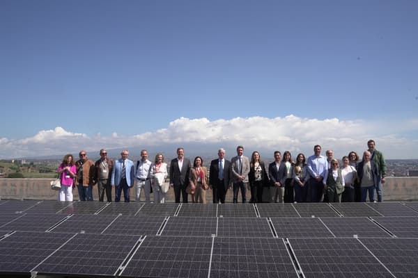 Un gruppo di persone su una terrazza dietro a dei pannelli solari.  