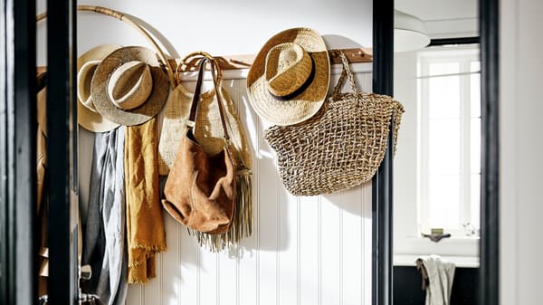 Un hall d’entrée blanc, une patère avec 6 boutons sur laquelle sont accrochés des sacs, chapeaux et foulards dans des tons naturels, et à côté, un miroir TOFTBYN.