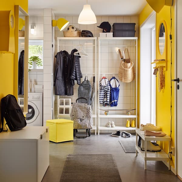 Un hall d’entrée lumineux en jaune et blanc avec un rangement blanc pour manteaux et chaussures.
