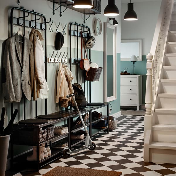 Un hall d’entrée traditionnel, avec un dallage noir et blanc, avec deux portemanteaux et deux rangements à chaussures noirs côte à côte.