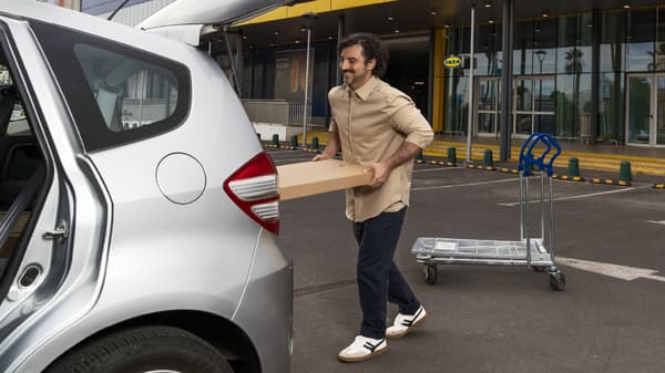 Un hombre cargando los paquetes planos de IKEA en el maletero de su auto.