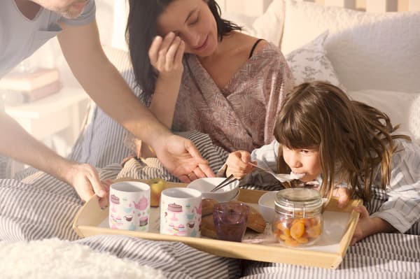 Un hombre, una mujer y una niña tomando desayuno en la cama sobre una bandeja.