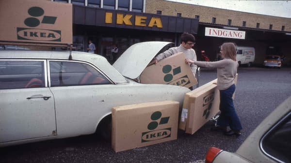 Un hombre y una mujer metiendo cajas planas de IKEA dentro de su auto blanco frente a la tienda.