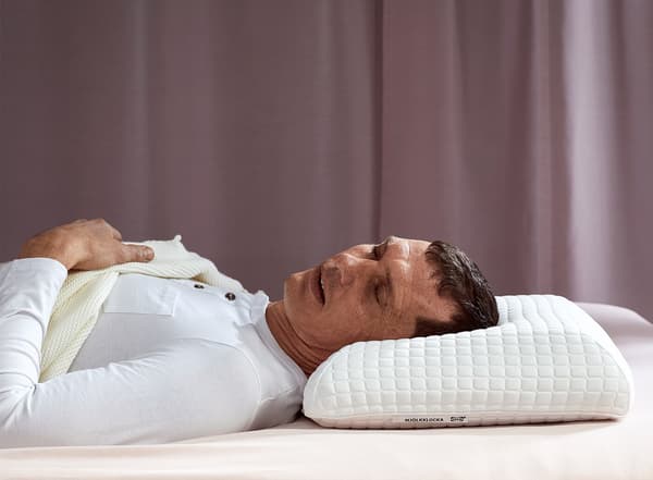Un home dorme placidamente de costas cunha almofada ergonómica IKEA MJÖLKKLOCKA.