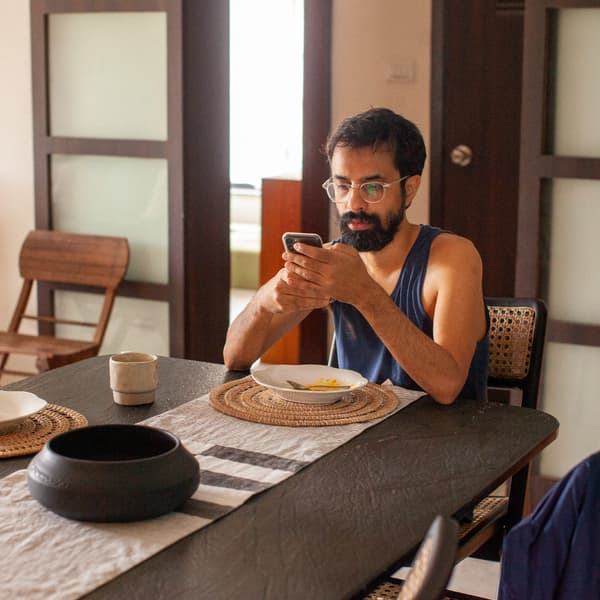 Un homme à la chevelure et à la barbe noires vient de terminer son repas ; il utilise son téléphone cellulaire assis à la table.
