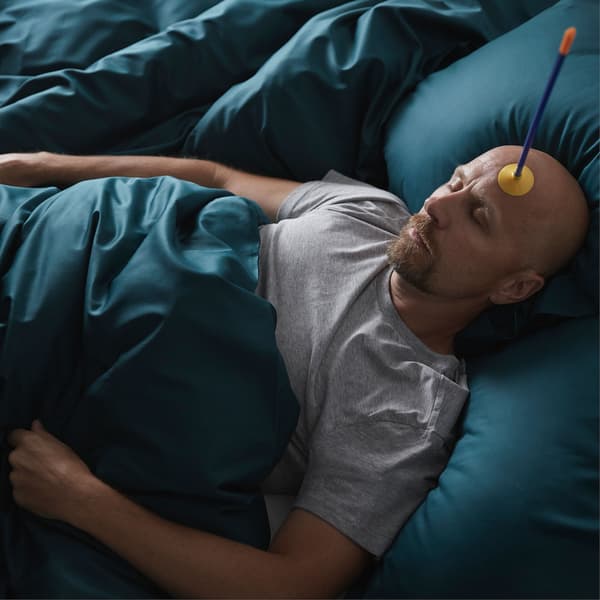 Un homme allongé sur un lit moelleux avec un jouet en forme de flèche collé sur son front.