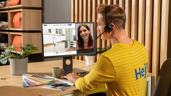 Un homme assis à un bureau en visioconférence avec une femme via un ordinateur portable. Sur un second écran, images de décors intérieurs.