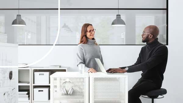 Un homme assis sur un tabouret et une femme debout discutent dans un bureau d'entreprise.