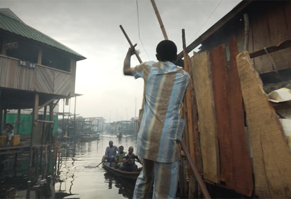 Un homme au costume coloré dirigeant une barque à travers un bidonville flottant en bois.