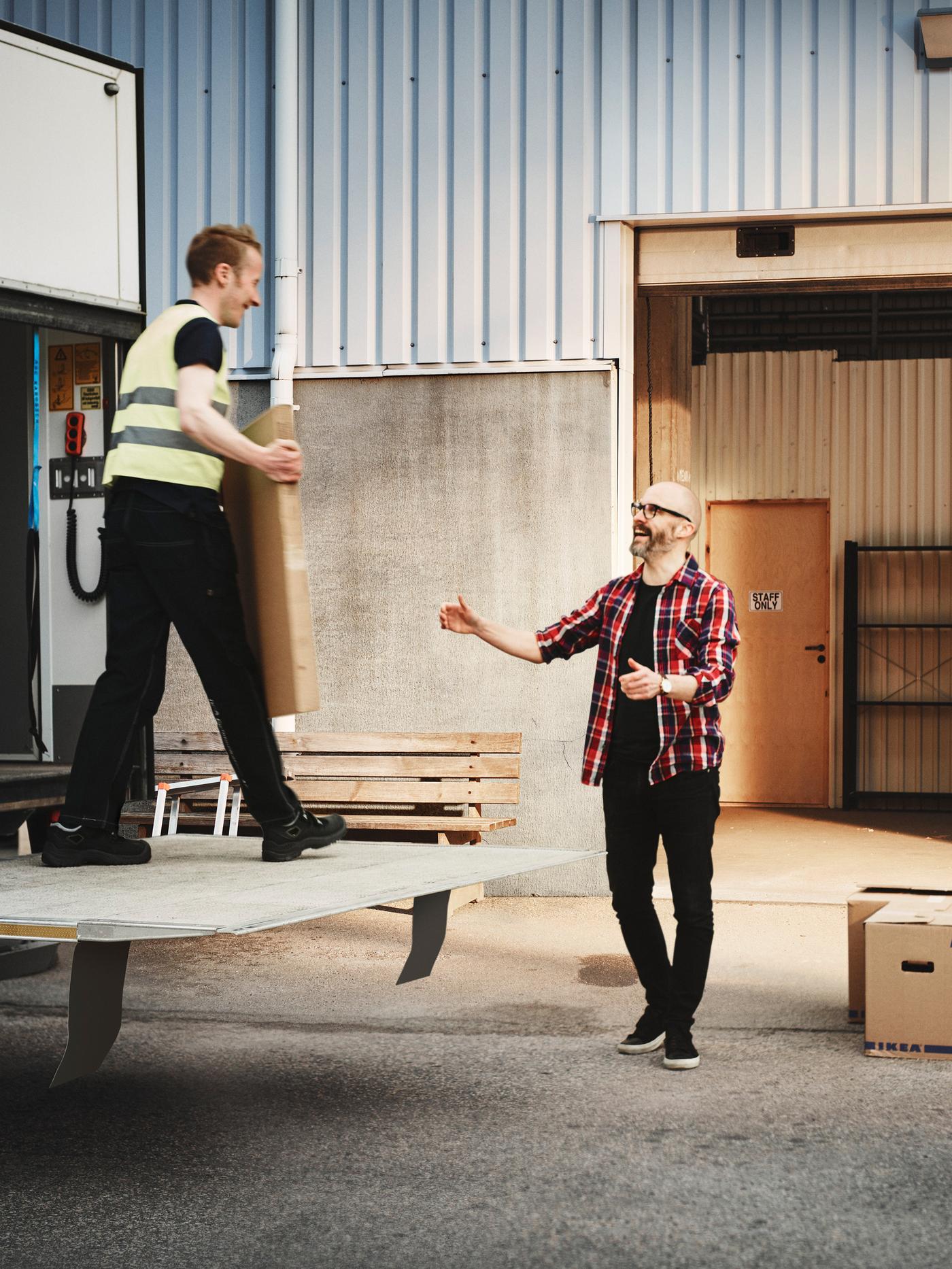 Un homme avec une barbe et des lunettes qui attend de prendre un article des mains d’un autre homme à l’arrière d’un camion de livraison.