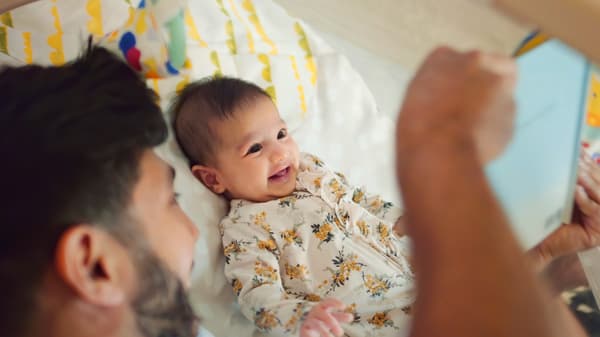 Un homme barbu amuse un bébé souriant sur un lit.