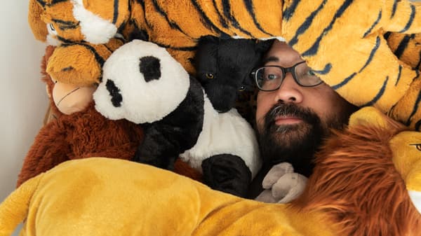 Un homme barbu portant des lunettes est étendu parmi plusieurs peluches DJUNGELSKOG. On ne voit que son visage.