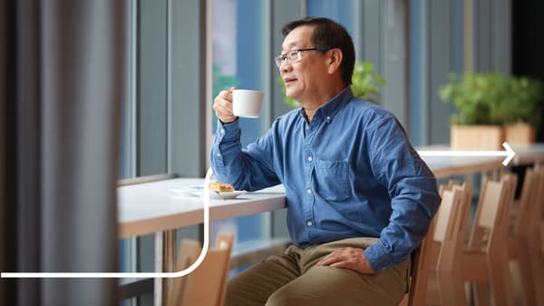 Un homme boit un café assis à un bar devant une grande fenêtre.