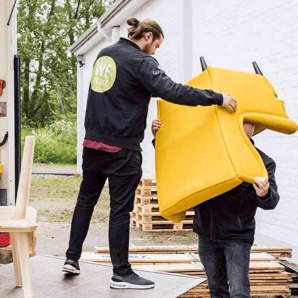 Un homme debout à l'arrière d'un camion passe un fauteuil jaune STRANDMON à une personne debout derrière le camion.