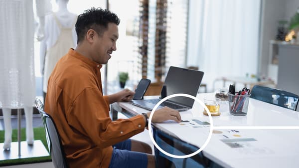 Un homme en chemise orange est assis à un bureau derrière son ordinateur portable