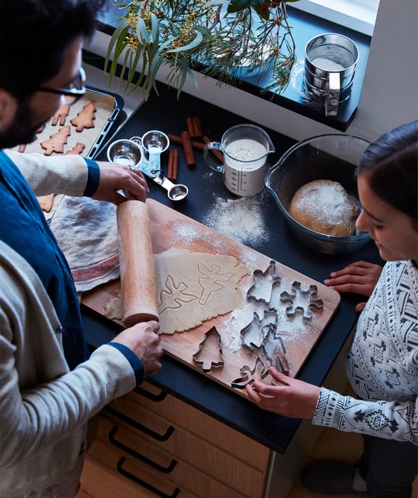 Un homme et une femme debout près d’un plan de travail de cuisine jonché de tous les signes d’une préparation de biscuits au pain d’épices.
