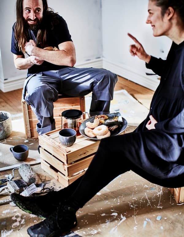 Un homme et une femme se regardent en riant; ils sont assis sur des caisses en bois pour une pause café en toute simplicité.