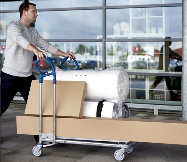 Un homme qui pousse un chariot IKEA avec plusieurs produits dedans.