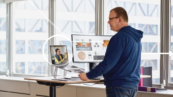 Un homme se tient debout derrière un bureau modulable en étant en visio avec une collaboratrice IKEA